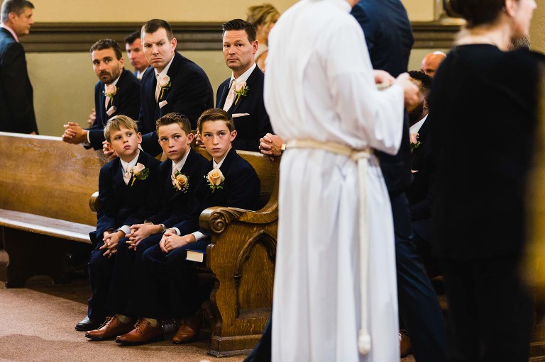 groomsmen boys and men with interesting expressions, while priest gives communion to congregation