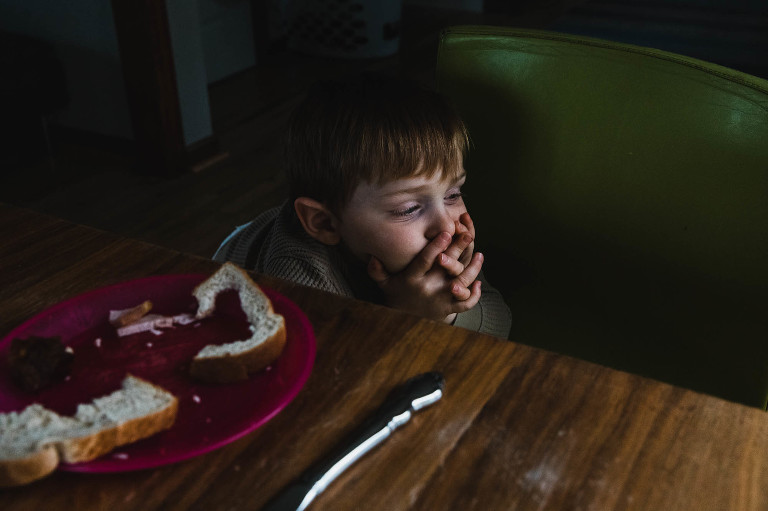 boy sits at dinner thoughtfully with his fingers crossed