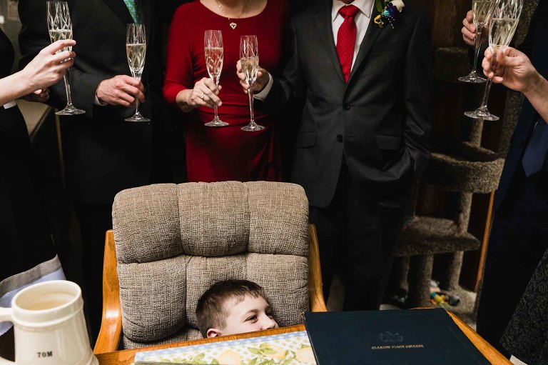 candid photo of boy hiding in a chair while the adults around him celebrate a special anniversary occasion.
