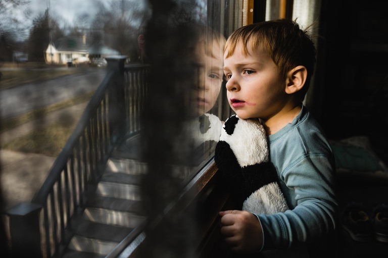 documentary photography picture of little boy sitting at the window